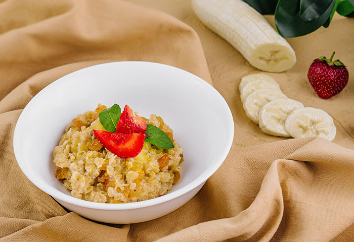 Tigela com frutas e aveia, ao fundo banana e morangos